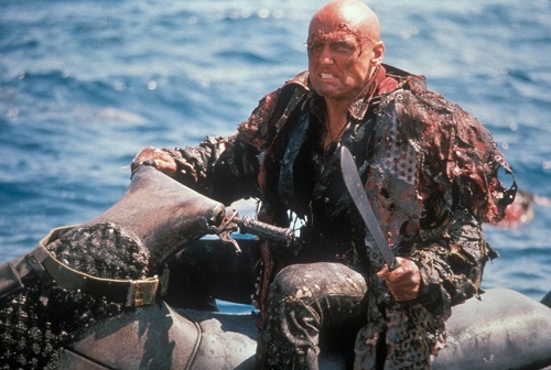 Dennis Hopper from the movie Waterworld riding a jet ski and wielding a machete.