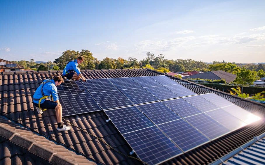 Two people installing solar panels on a roof.