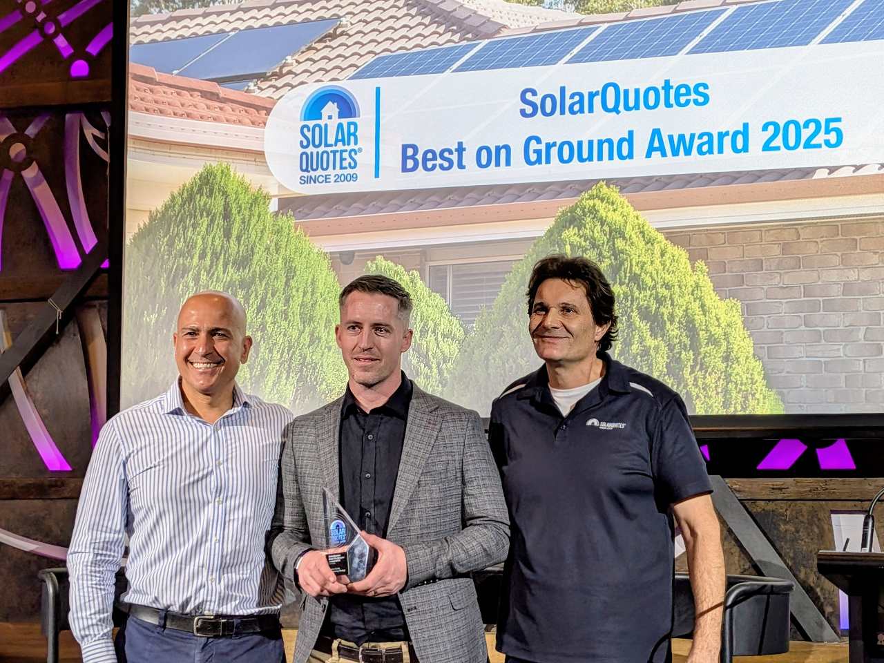 Three men on stage, with one holding an award.