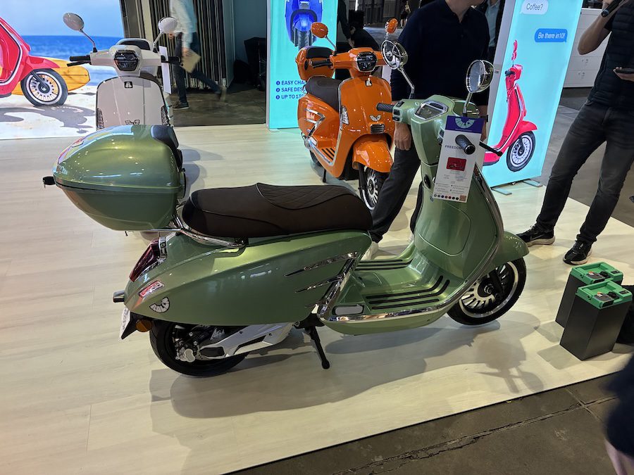 Green electric scooter on a stage with man's legs in background.