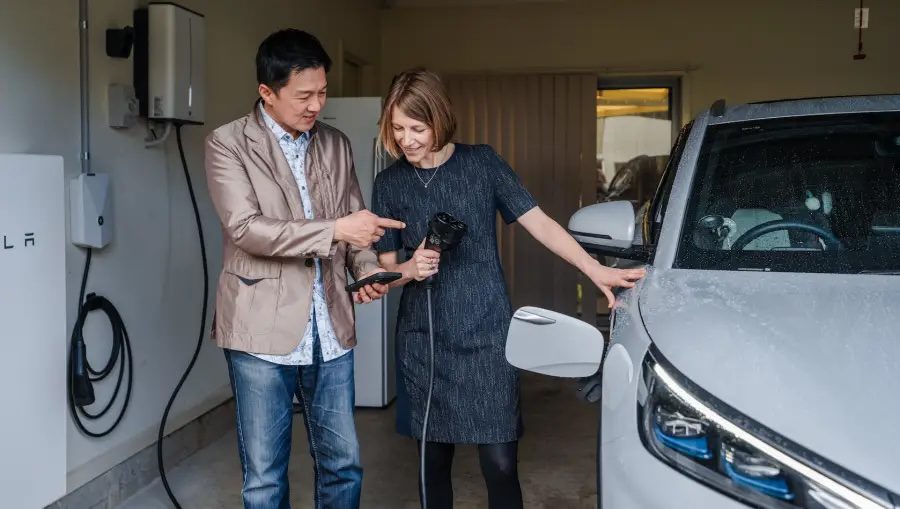 Man and woman looking at a smart phone while plugging in a charger into an EV.