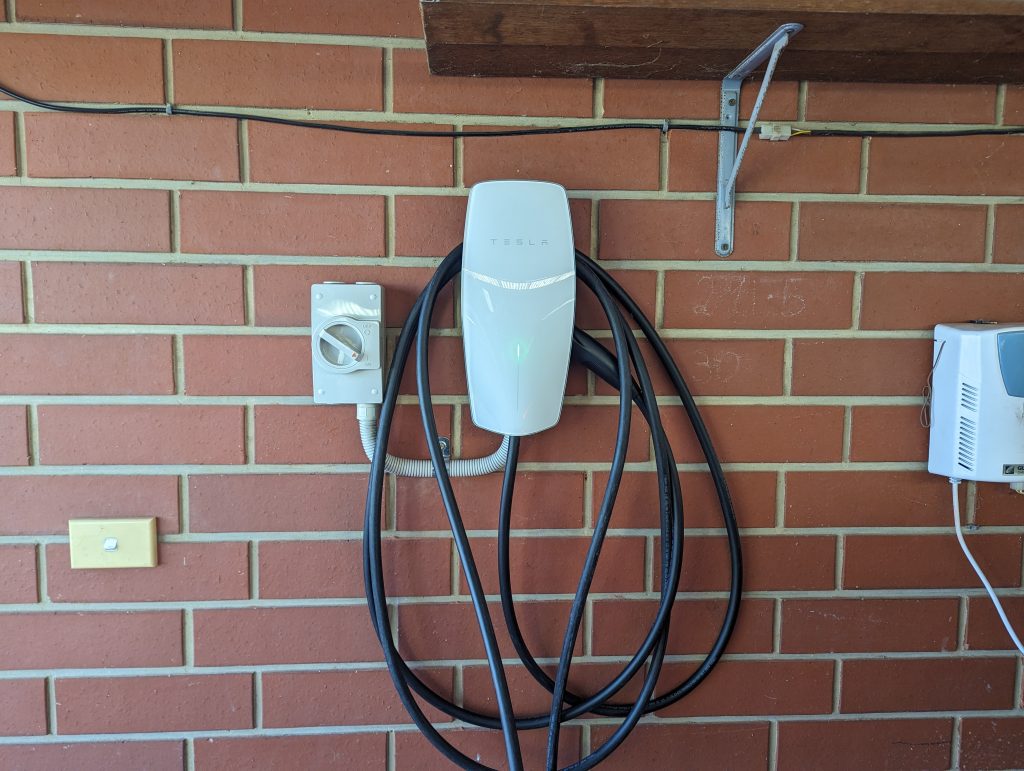 A Tesla Wall connector installed on a garage wall next to an isolator