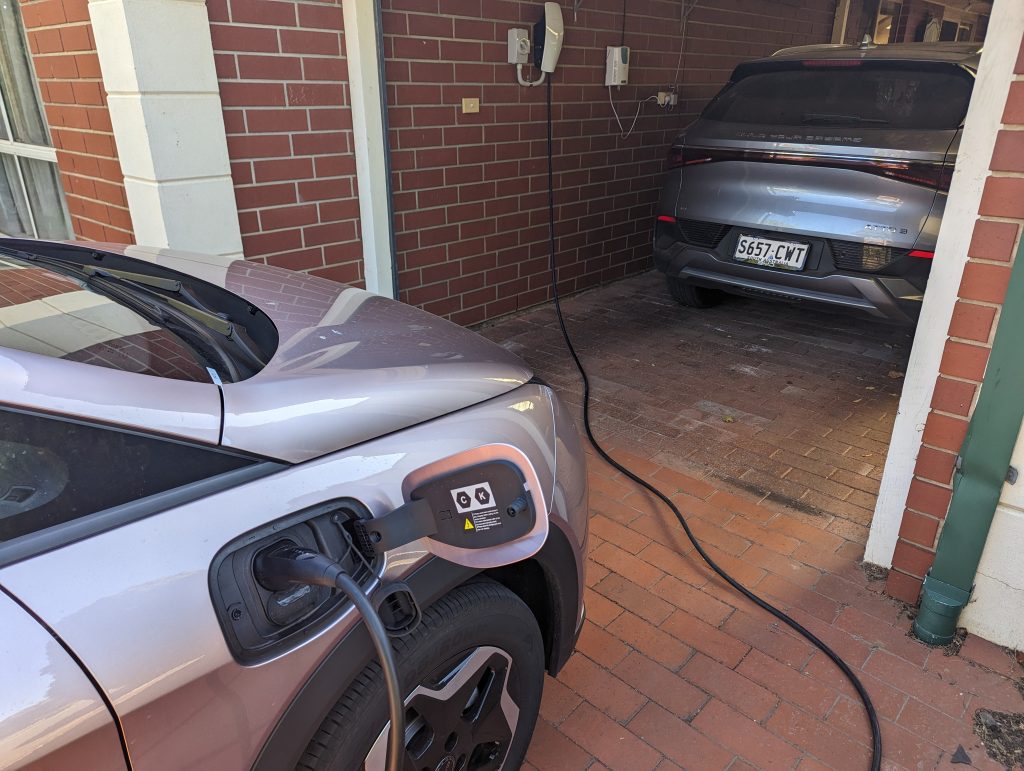 A Tesla Wall Connector charging an EV in the driveway