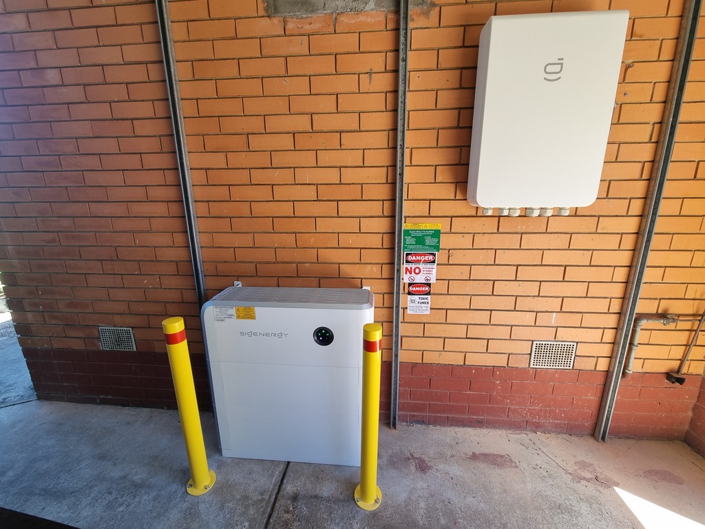 A SigenStor home battery installed in a garage behind bollards.
