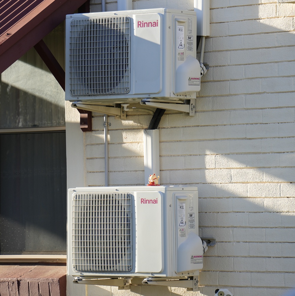Two Rinnai outdoor compressor units mounted on a brick wall, showing a typical split-system air conditioner setup. Each unit serves its own indoor head, unlike a multi-split system which uses one outdoor unit for multiple rooms.
