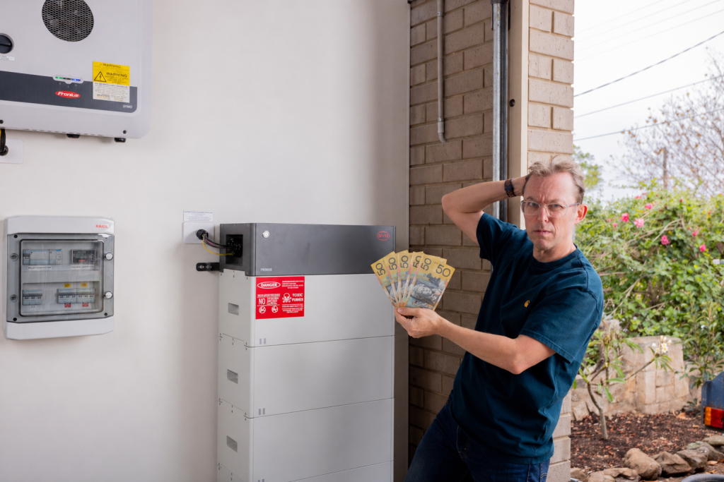 Finn Peacock holding money in front of a home battery.